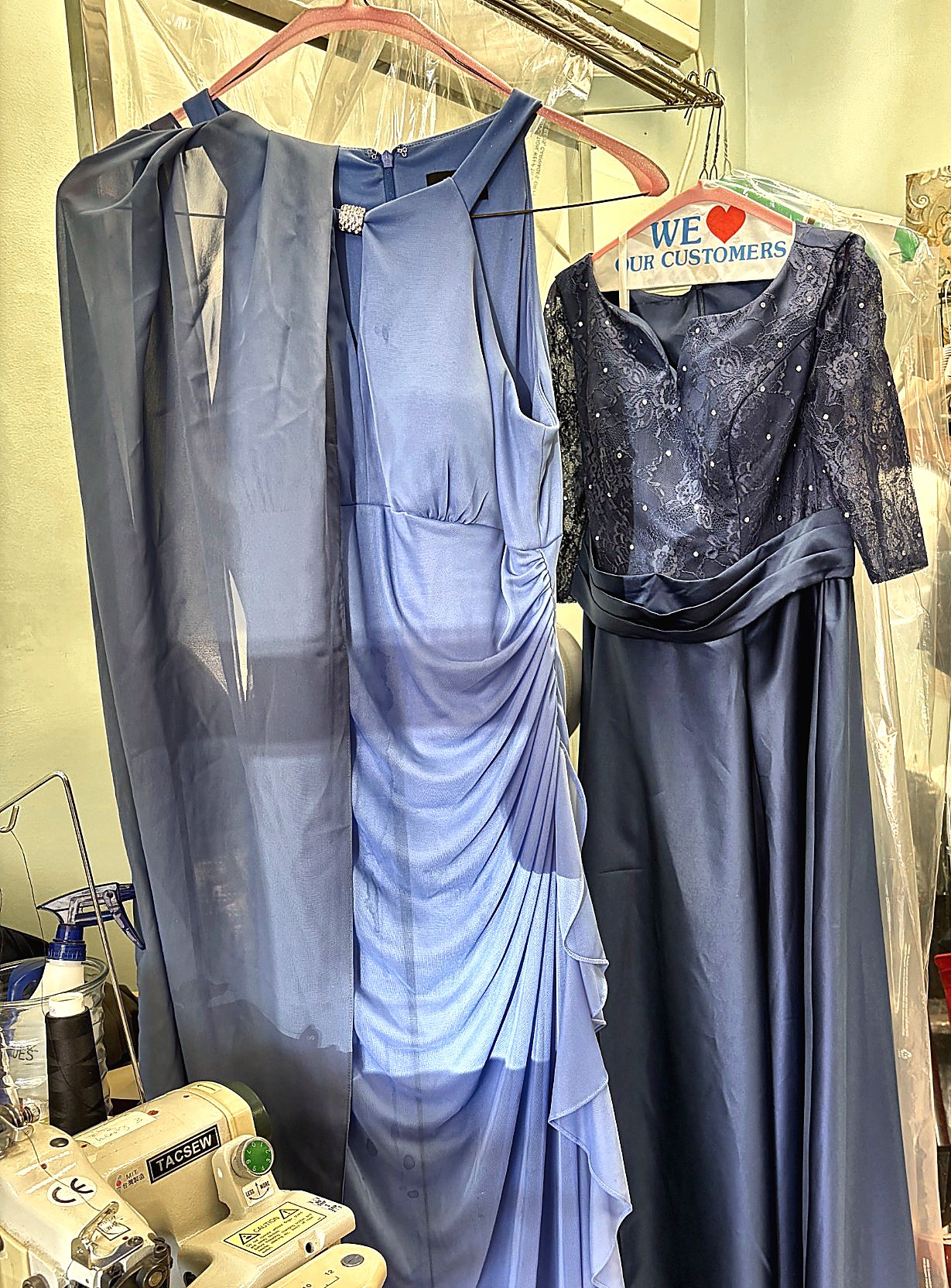 Two formal gowns hanging in the shop next to a hemming machine